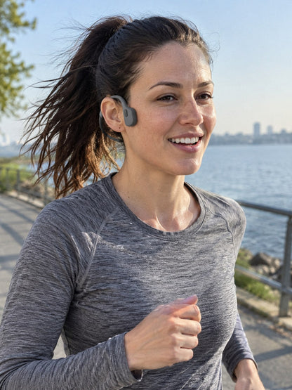 A woman running on a waterfront path wearing the ECDF Open-Ear Swim Headphones