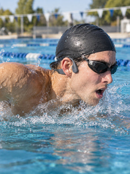 A swimmer doing laps in an outdoor pool wearing the ECDF Open-Ear Swim Headphones under his swim cap strap, pads in front of his ears